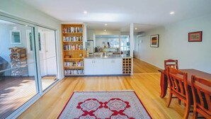 A modern kitchen with white cabinets, a central island, and a dining area with wooden chairs. - 150  Steps to Beach with EV Charging (Apollo Bay)