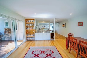 A modern kitchen with white cabinets, a central island, and a dining area with wooden chairs. - 150 Steps to Beach with EV Charging (Apollo Bay)