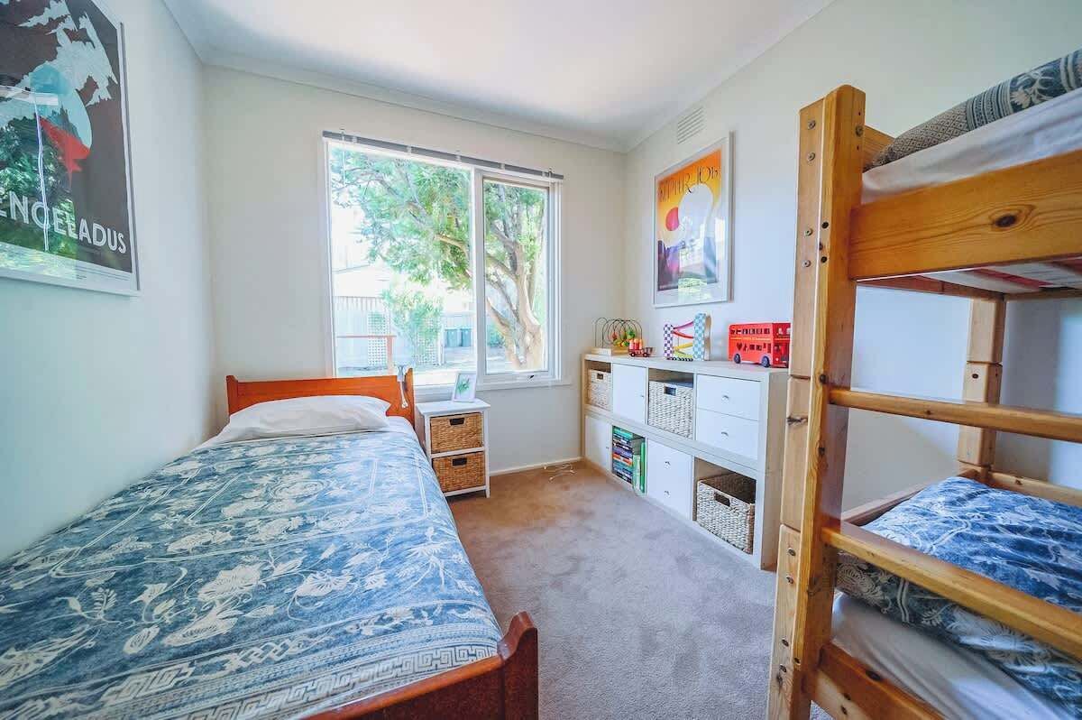 A bedroom with a bed, a bunk bed, a window with a view, a desk with storage, and a poster on the wall.
