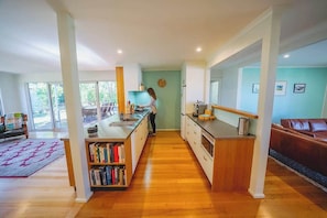 A modern kitchen with a central island, a dining area with a brown leather couch, and a view of the outdoors through large windows. - 150  Steps to Beach with EV Charging (Apollo Bay)