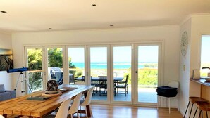 A spacious room with a large wooden table, white chairs, and a view of the ocean through sliding glass doors. - Apollo Ocean Blue Ocean View Wi-Fi Pet Friendly (Apollo Bay)