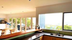 A modern kitchen with a large window, wooden cabinets, and a built-in dishwasher. - Apollo Ocean Blue Ocean View Wi-Fi Pet Friendly (Apollo Bay)