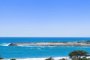 Vista costera con costa rocosa, cielo azul despejado y un muelle distante.