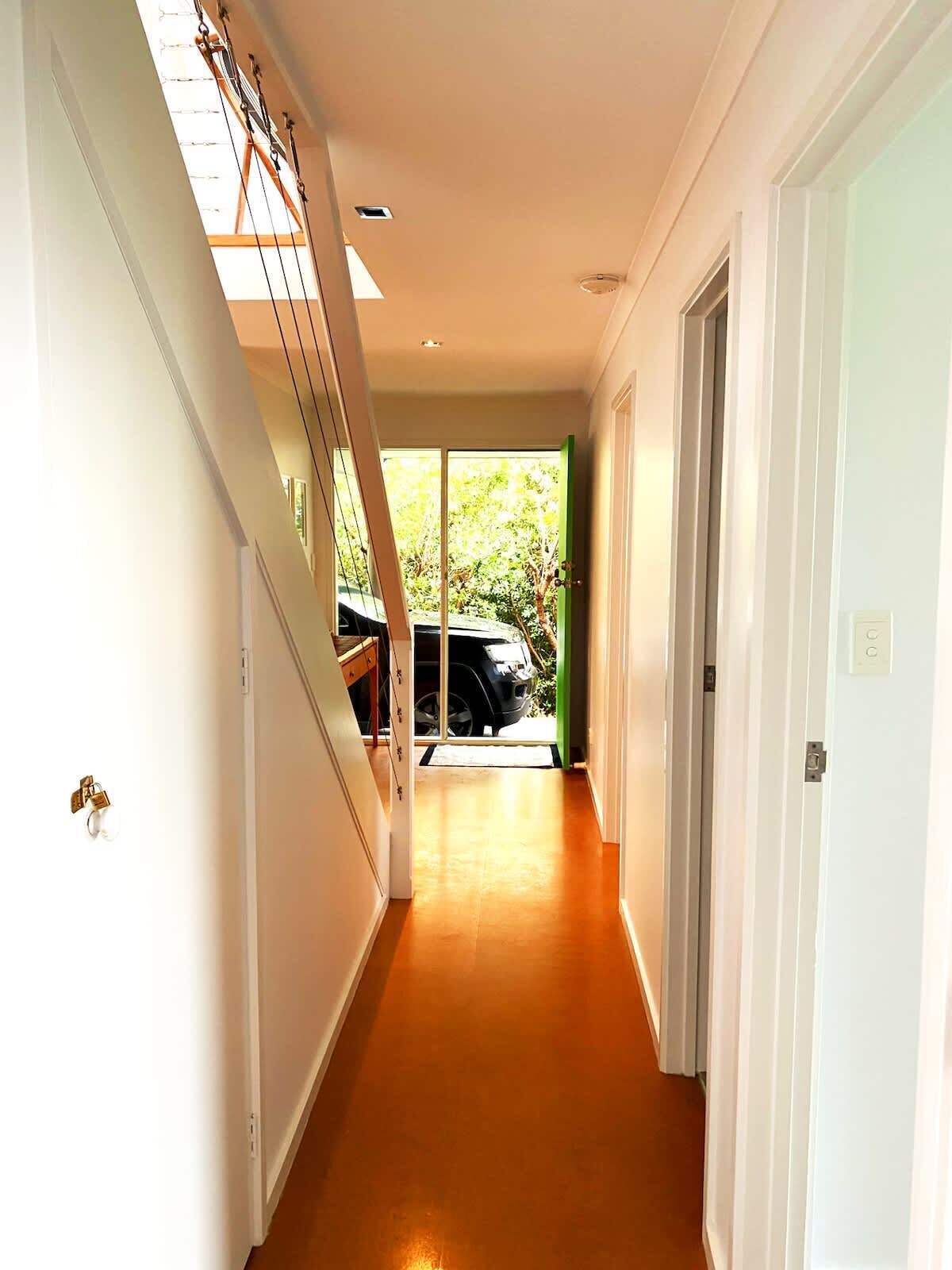 A hallway with a staircase on the left, a door on the right, and a view of a car outside.