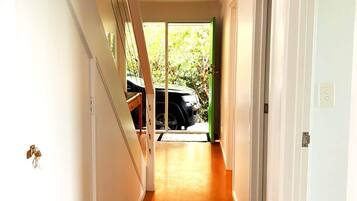 A hallway with a staircase on the left, a door on the right, and a view of a car outside.