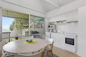 A kitchen with white cabinets, a microwave, a stove, and a dining table with chairs. - Bay Beach Studio Opposite the Beach and Main Shops (Apollo Bay)
