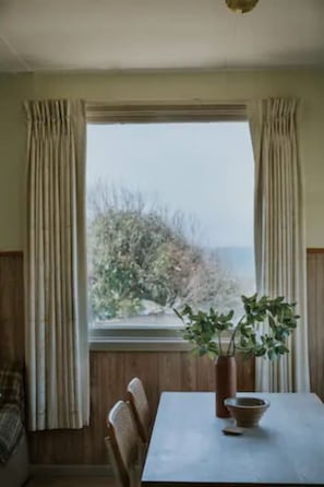 Enjoy a serene view from the large window, featuring a table and a vase with a plant.