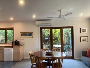 Eine moderne Küche mit Geschirrspüler, einem Esstisch mit Stühlen, einem Deckenventilator und einer Glastür zum Außenbereich.