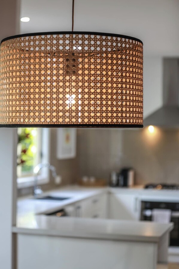 Cocina moderna con isla central, iluminación colgante y estufa a la vista.