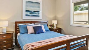 Une chambre à coucher avec un lit, des tables de chevet, un tableau encadré et une fenêtre.
