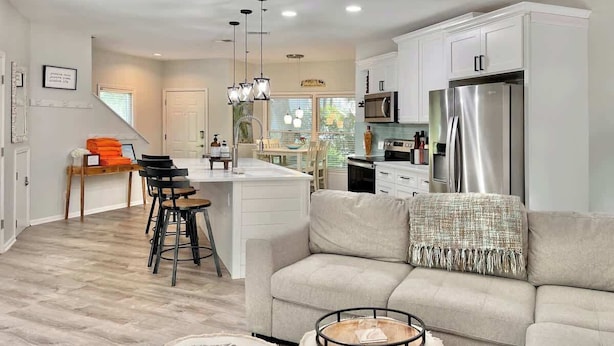 A modern kitchen with white cabinets, a stainless steel refrigerator, and a dining area with a wooden table and chairs.