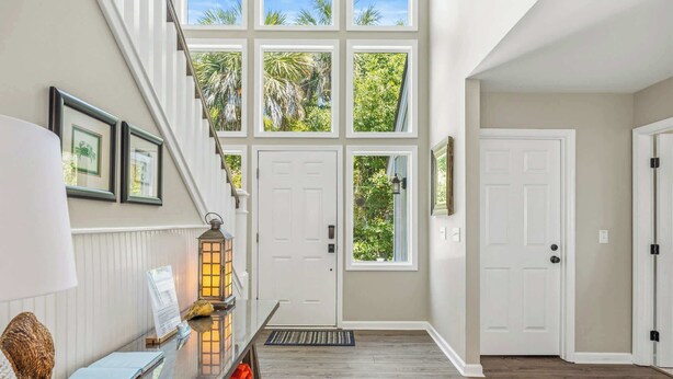 A hallway with a staircase, a door with a view of greenery, and a wall-mounted lantern.