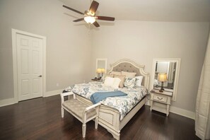 A bedroom with a bed, a bench, a ceiling fan, a nightstand, a mirror, and a door.