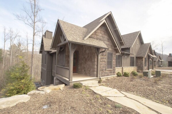 A residential building with a stone facade, a covered porch, and a landscaped yard with mulch and stepping stones.