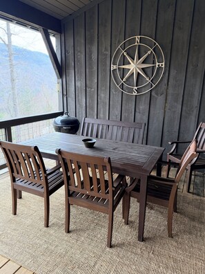 A wooden deck with a table and chairs, a compass wall decoration, and a view of the mountains.