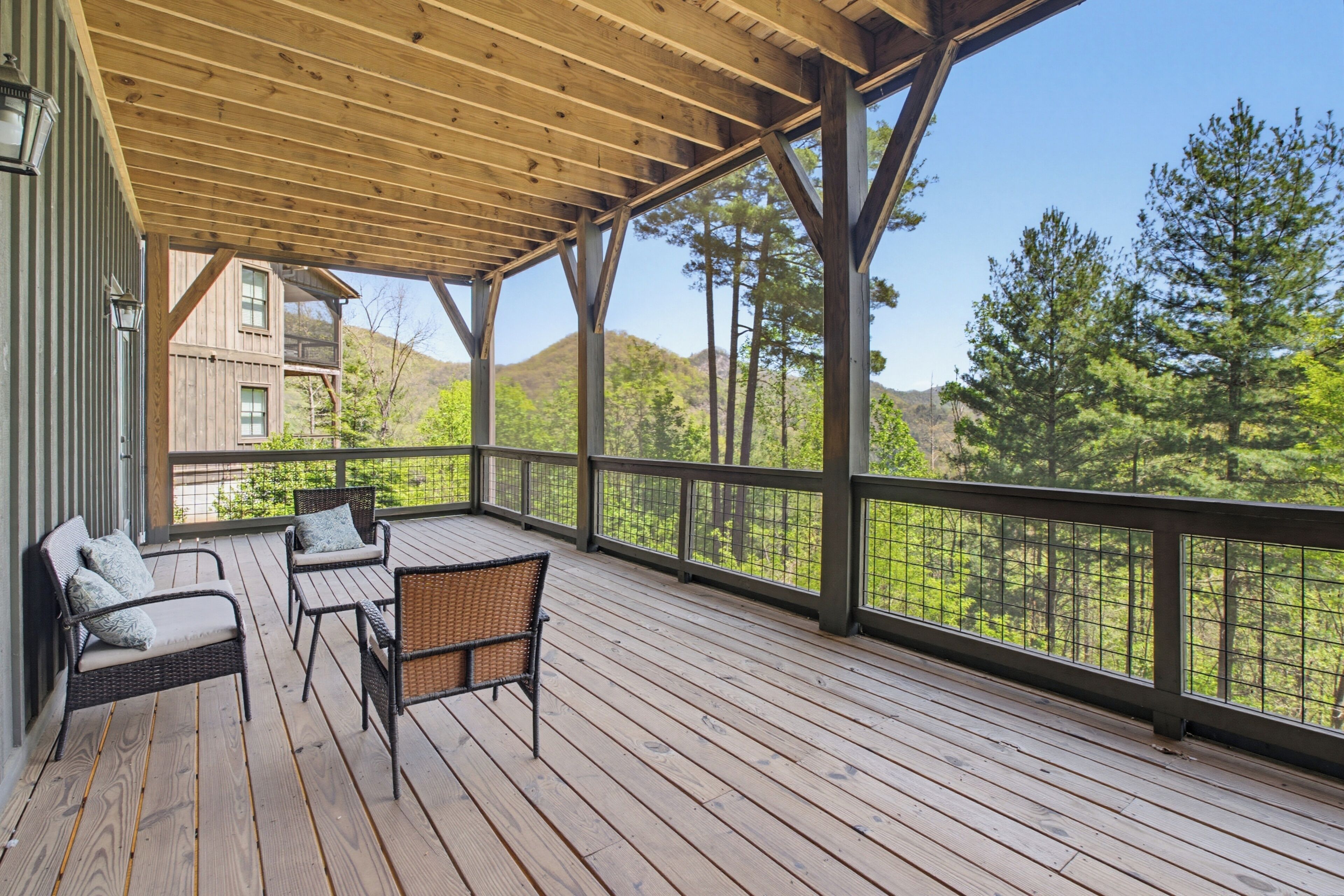 Eine Holzterrasse mit Gartenmöbeln, einem Geländer und Blick auf Bäume und Hügel.