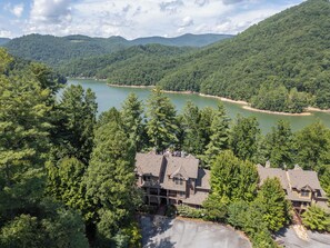 Ein großes Haus mit einer breiten Auffahrt und Blick auf einen See, der von bewaldeten Hügeln umgeben ist.