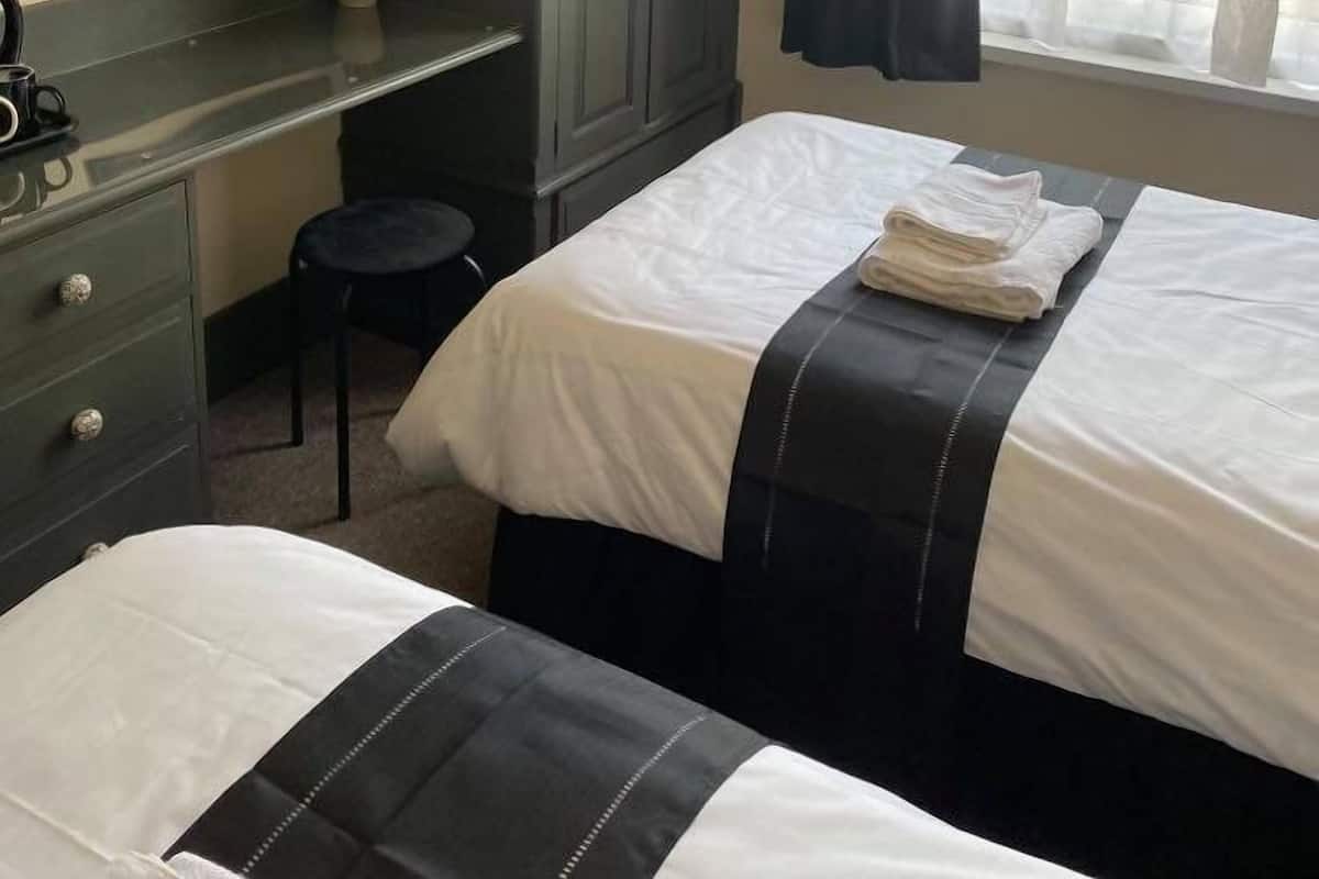 A hotel room with two beds, a desk, a wardrobe, and a window with curtains.