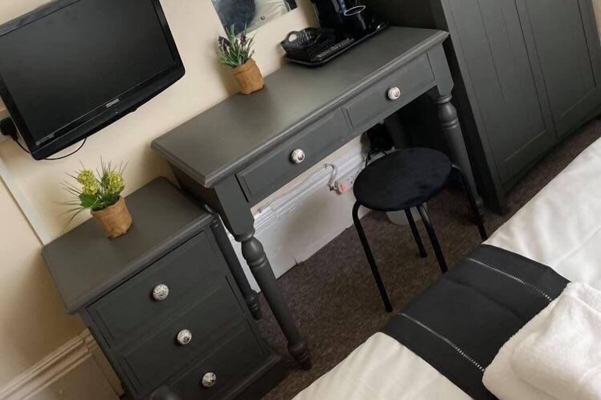 A bedroom with a bed, a desk with a computer, a chair, a wardrobe, and a small plant.