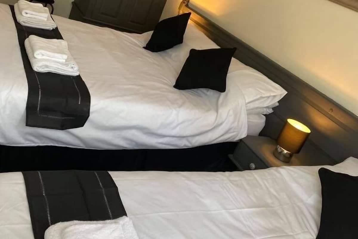 A hotel room with two beds, each with white linens and black pillows. There is a wooden wardrobe, a mirror, and a framed picture on the wall.
