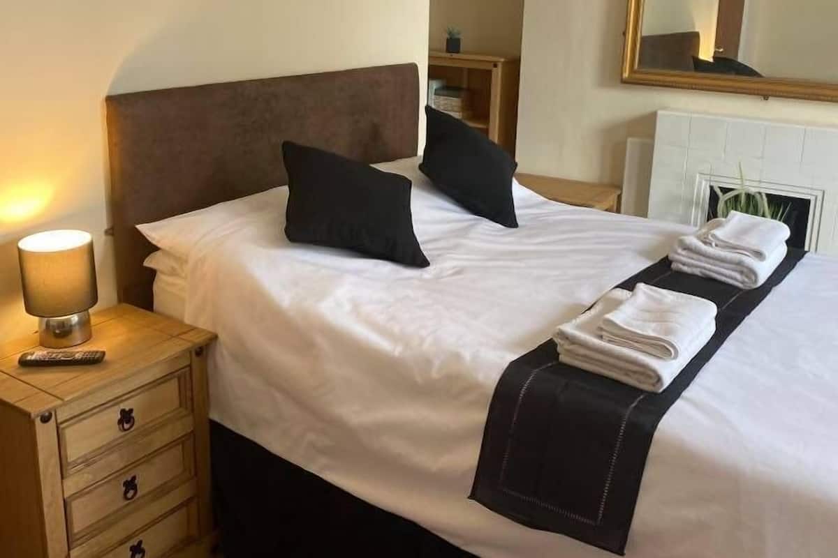 A neatly made bed with a headboard, a bedside table with a lamp, and a mirror on the wall.