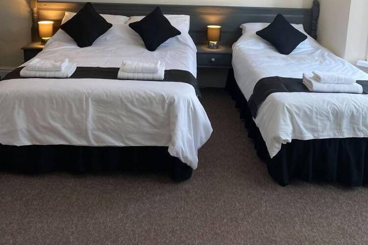 A hotel room with two single beds, each with a black headboard, white bedding, and a framed picture on the wall.
