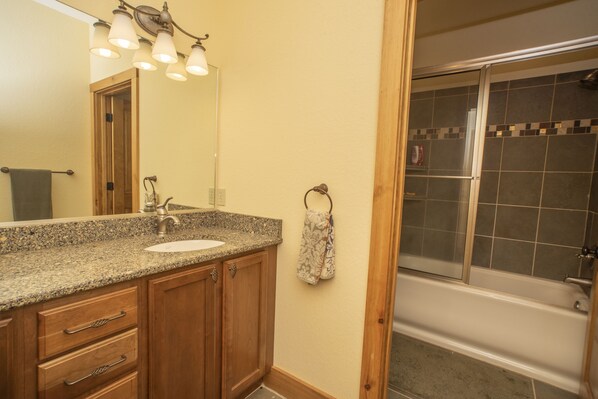 A bathroom with a granite countertop sink, wooden cabinets, a towel rack, and a shower area. - 1449 Lake Forest Drive at Bear Lake Reserve (Tuckasegee)