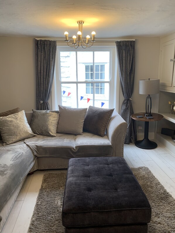 A living room with a sofa, ottoman, and a lamp on a table.