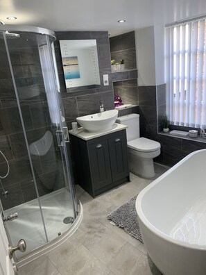 Un bany modern amb una cabina de dutxa de vidre, una banyera independent, un lavabo blanc i un vàter.