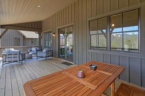 Eine Holzdielen-Terrasse mit Tisch und Stühlen, großen Fenstern und Blick auf ein Gebäude im Hintergrund.