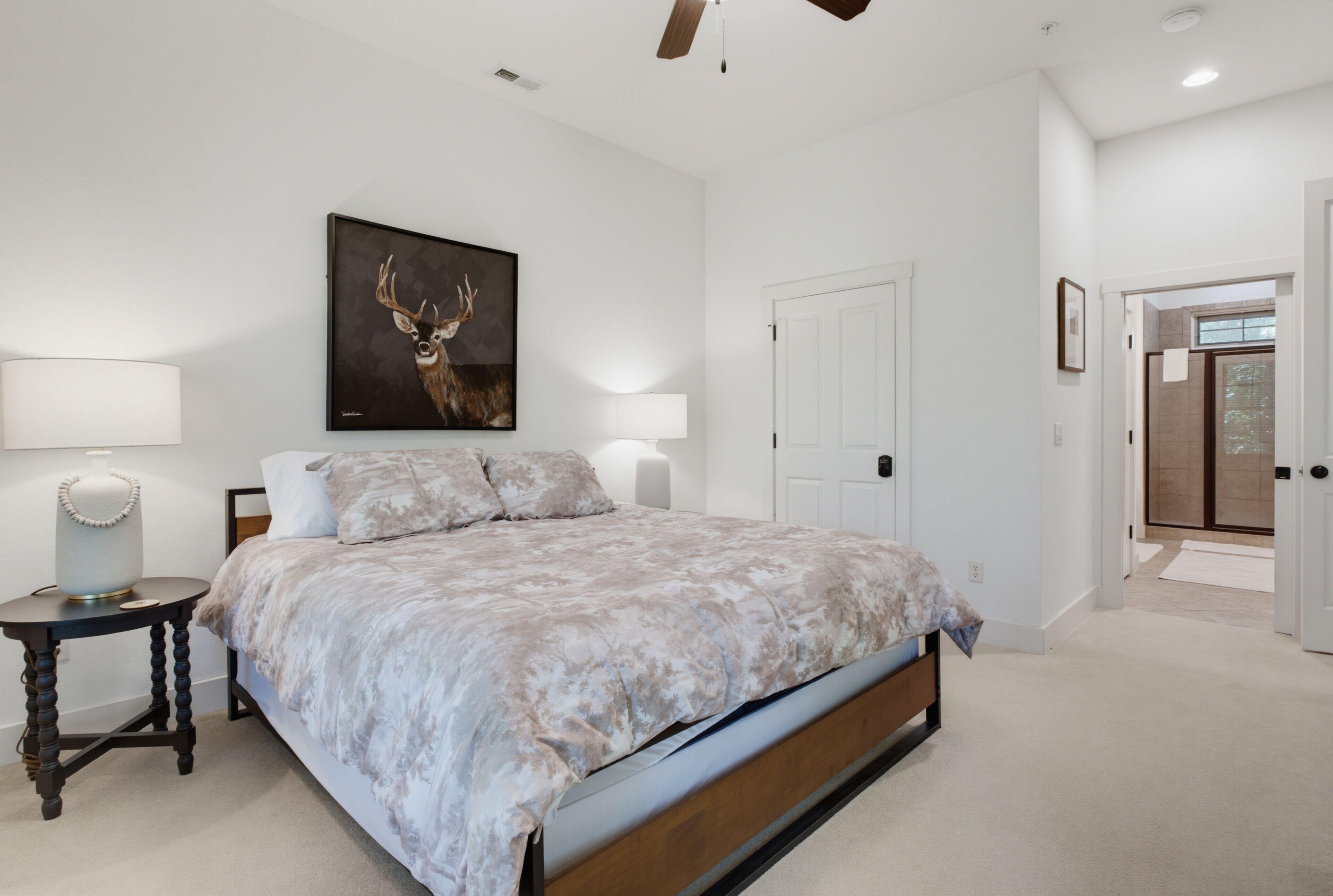 Een slaapkamer met een bed, een schilderij van een herten aan de muur, een deur en een gang naar een andere kamer.