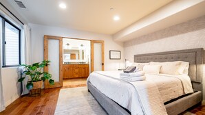 A modern bedroom with a large bed, a wooden floor, a potted plant, and a bathroom visible through an open door. - Walk to the Beach/Rooftop Deck with Views/7 beds- 2 Kings/ A/C (Encinitas)