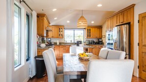A modern kitchen with wooden cabinets, a central island, and a dining area with white chairs. - Walk to the Beach/Rooftop Deck with Views/7 beds- 2 Kings/ A/C (Encinitas)