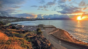 Une vue sur la côte au coucher du soleil, avec une promenade pavée et un petit port abritant des bateaux.