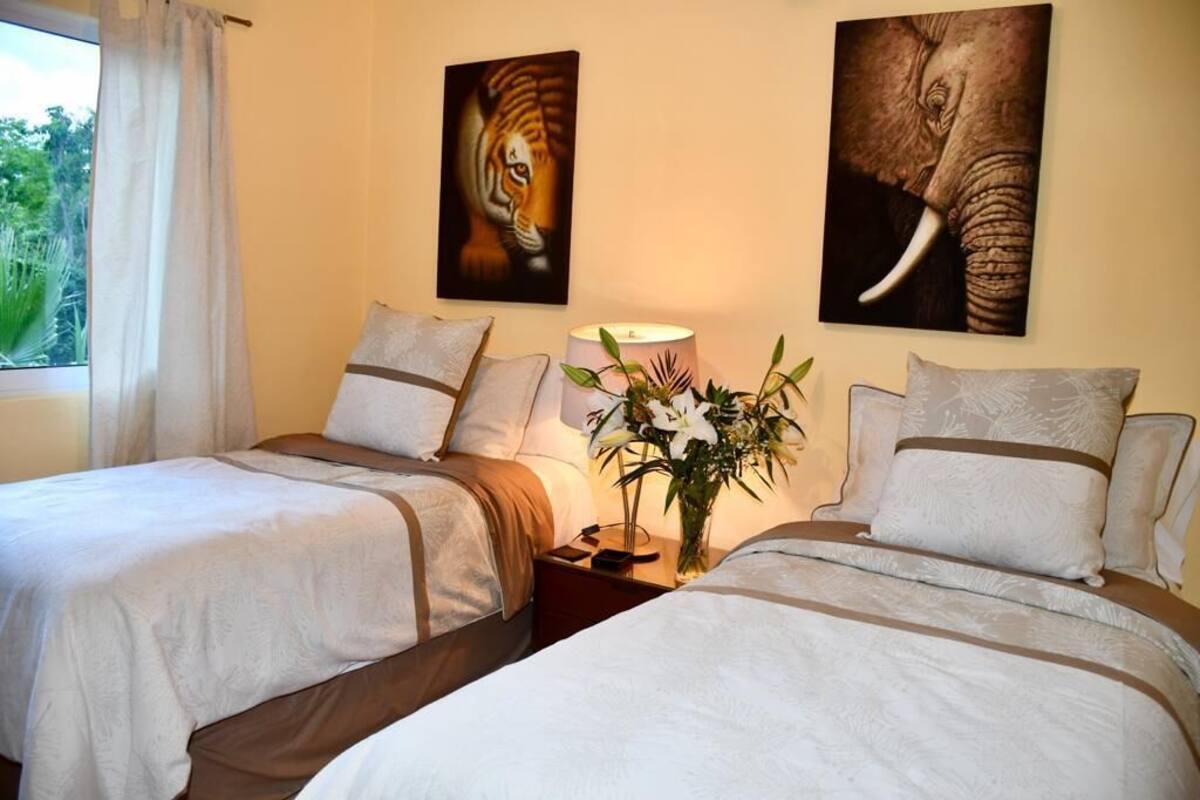 Ein Hotelzimmer mit zwei Betten, einem Nachttisch mit Lampe und Blumenvase sowie zwei Bildern an der Wand.