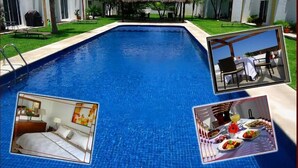 Piscina com uma estrutura de telhado de palha no centro, rodeada por edifícios brancos com detalhes amarelos.