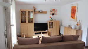 Una sala de estar con sofá, televisión, armarios de madera y un reloj de pared.