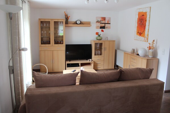 Una sala de estar con sofá, televisión, armarios de madera y un reloj de pared.