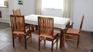 Un área de comedor con una mesa y sillas de madera, una cocina al fondo y una ventana con cortinas.