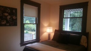 A bedroom with a bed, a nightstand with a lamp, and two windows with views of greenery. - Craftsman Duplex in Old Town Issaquah - Free Wi-Fi (Issaquah)