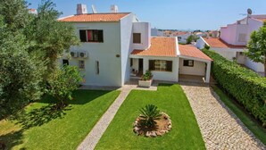 Une villa blanche avec un toit en tuiles, une allée pavée et une pelouse bien entretenue agrémentée d’un jardin central.