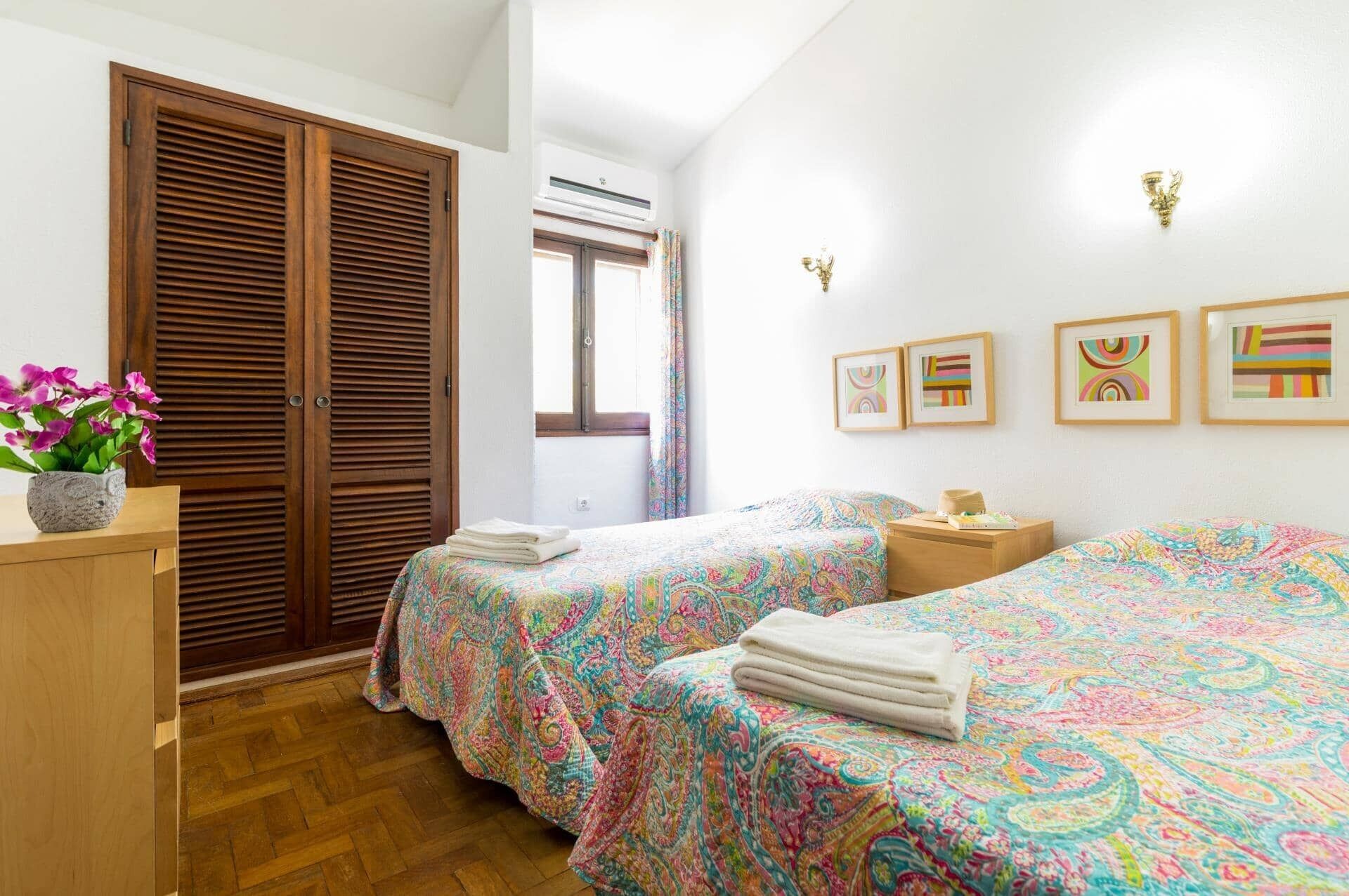 Un dormitorio con dos camas, un armario de madera, un ventanal con cortinas y obras de arte colgadas en la pared.