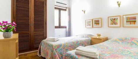Un dormitorio con dos camas, un armario de madera, un ventanal con cortinas y obras de arte colgadas en la pared.
