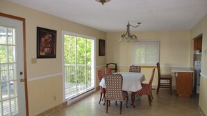 A dining area with a table and chairs, a kitchen area with a stove, and a large window with a view of greenery. - Puslinch Lake Waterfront (Puslinch)