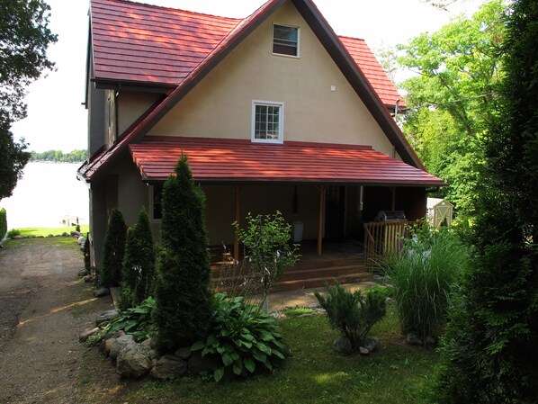 Una casa de dos pisos con techo rojo, un porche cubierto y vista a un lago.