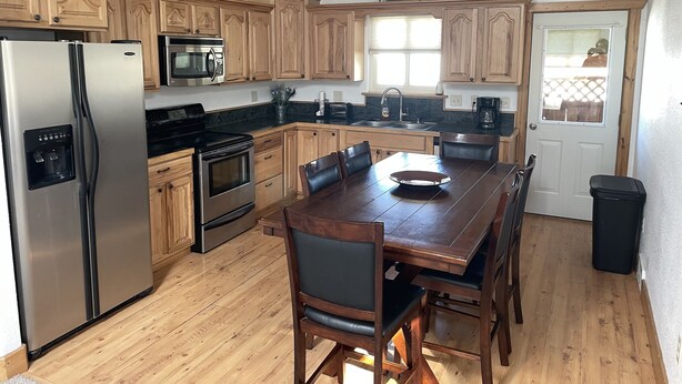 A kitchen with wooden cabinets, stainless steel appliances, a dining table with chairs, and a window. - Beartracks Retreat (Dubois)