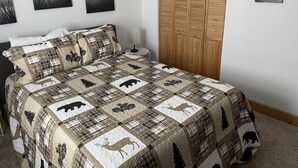 A bedroom with a bed, a nightstand, a wooden wardrobe, and wall art. - Beartracks Retreat (Dubois)