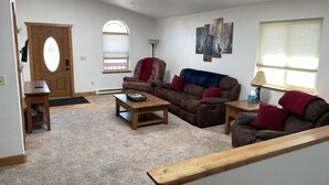 A living room with a brown sofa, a wooden coffee table, and a red armchair. There is a door with a window, a lamp, and a painting on the wall. - Beartracks Retreat (Dubois)