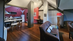 Una cucina moderna con una parete di accento rossa, una zona pranzo con uno sgabello da bar e un soggiorno con divano in pelle e una lampada.