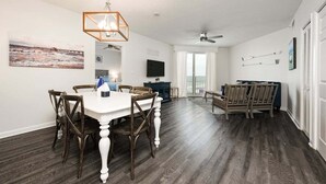 A spacious living room with a dining area, hardwood flooring, a ceiling fan, and a large window. - Ocean View Oasis - Ocean Walk (Daytona Beach)